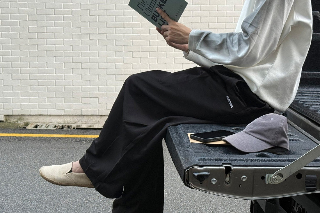 Man in a SAMA White Ribbed Long Sleeve and Black Baggy Trousers sitting on a truck tailgate outdoors